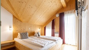 Ein Zimmer mit Holzboden, einem Bett, einer Bank und einem Fenster mit Vorhängen.