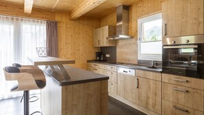 Eine moderne Küche mit Holzausbau, einer zentralen Kochinsel, Barhocker, einer Edelstahl-Dunstabzugshaube und einem großen Fenster.