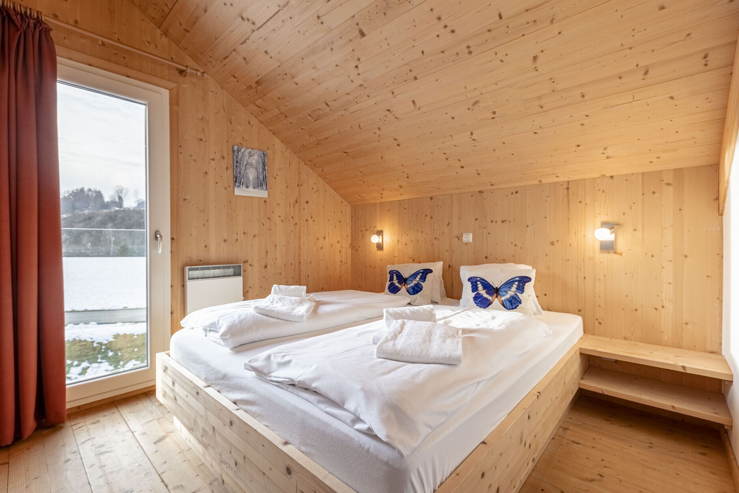 Un dormitorio tipo cabaña de madera con dos camas, una ventana con cortinas y vistas a un paisaje nevado.