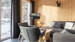 Ein gemütliches Wohnzimmer mit großem Fenster, Flachbildfernseher und einem aufgehängten Hirschkopf an der Wand.