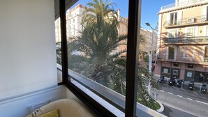 Quarto com uma janela grande que dá para a rua, com edifícios e scooters estacionados.