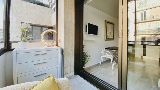 Quarto moderno com toucador, espelho, televisão e vista para a cidade através de grandes janelas.