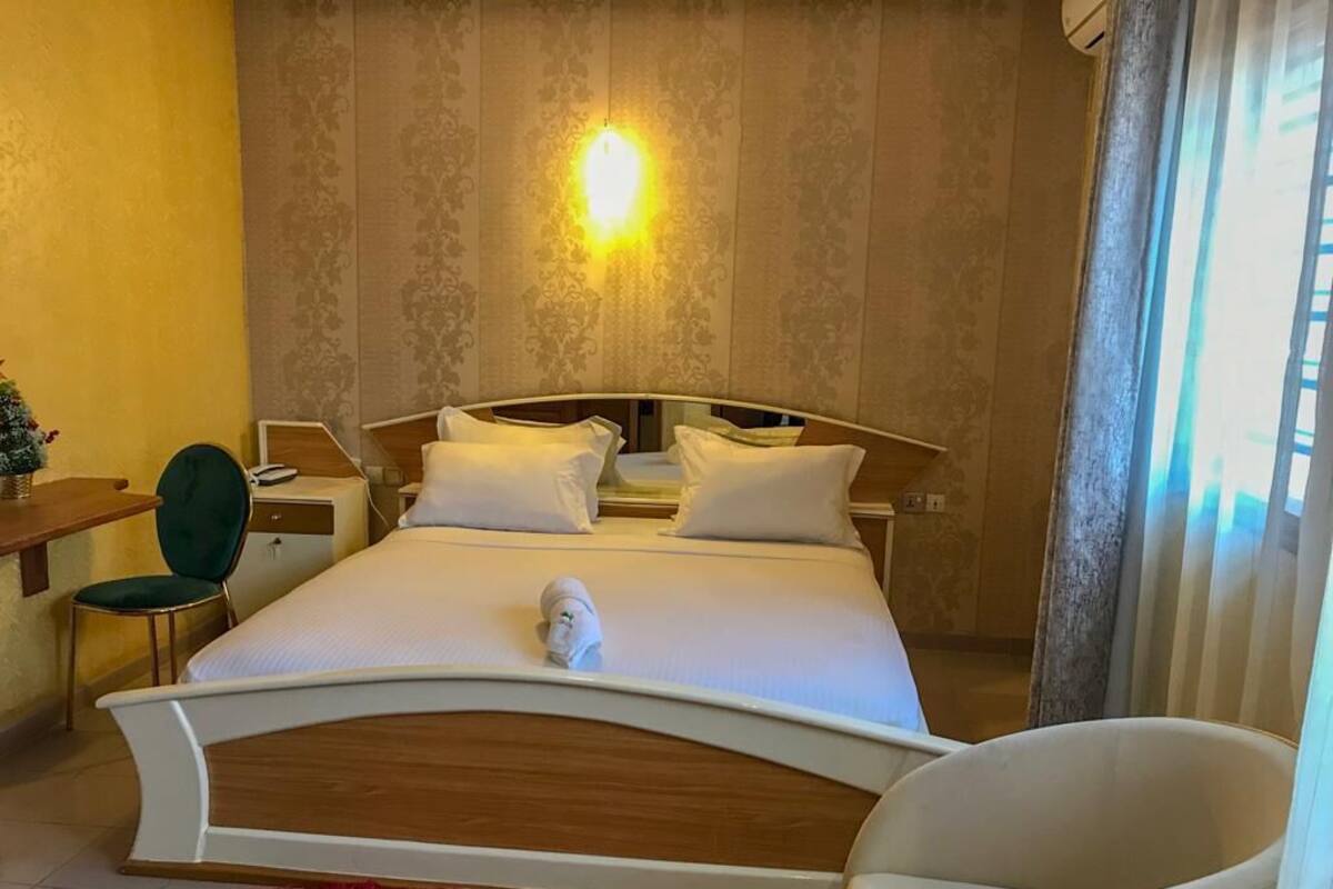 A hotel room with a bed, a chair, a desk, and a nightstand.
