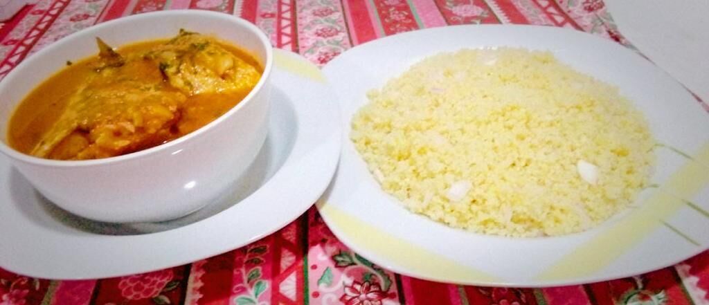 A white bowl of curry and a plate of rice on a table with a floral tablecloth.