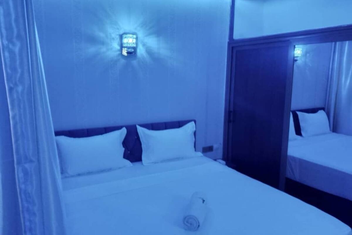 A hotel room with a bed, a nightstand, and a wall-mounted light fixture.