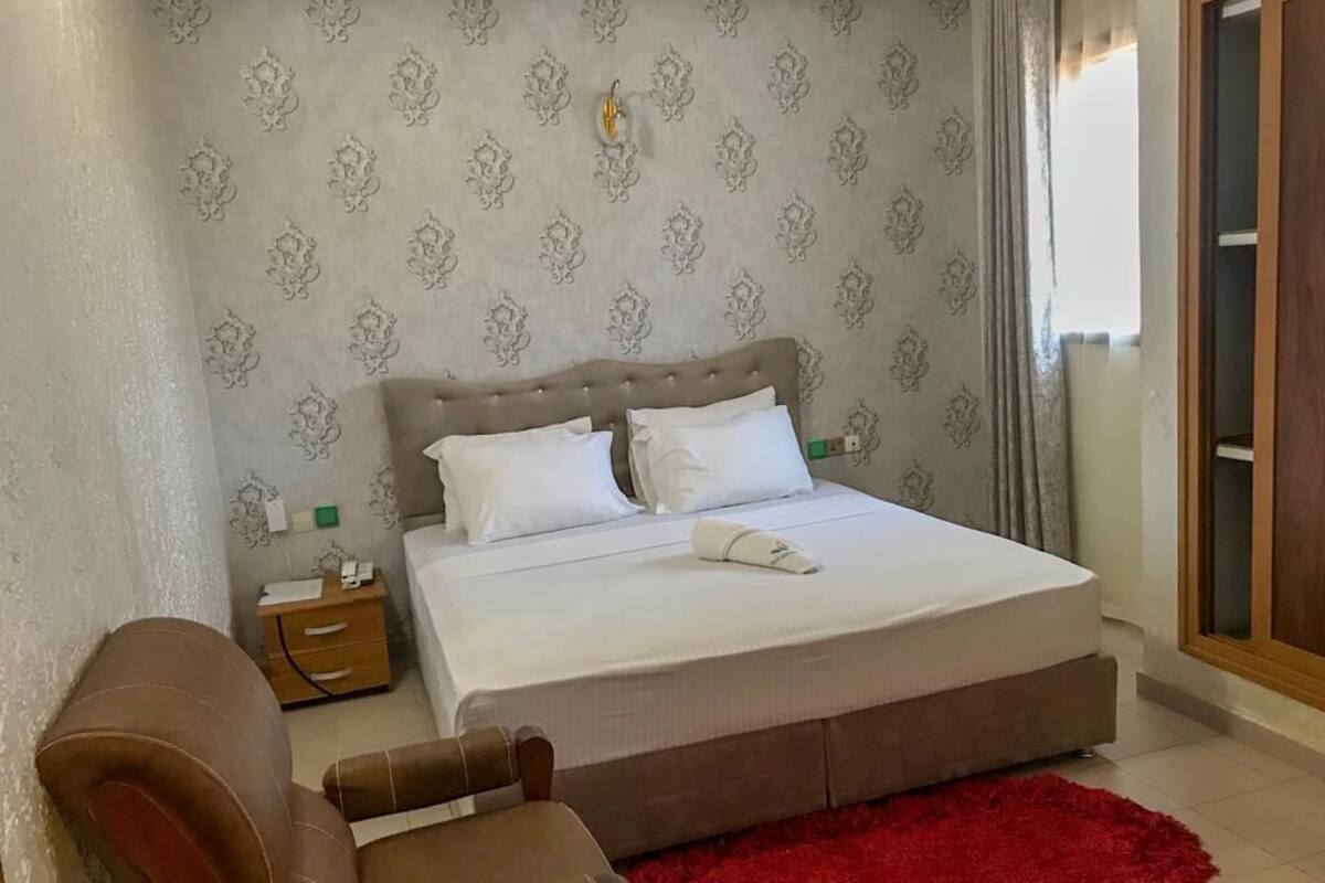 A bedroom with a large bed, a nightstand, a brown leather chair, and a red rug.