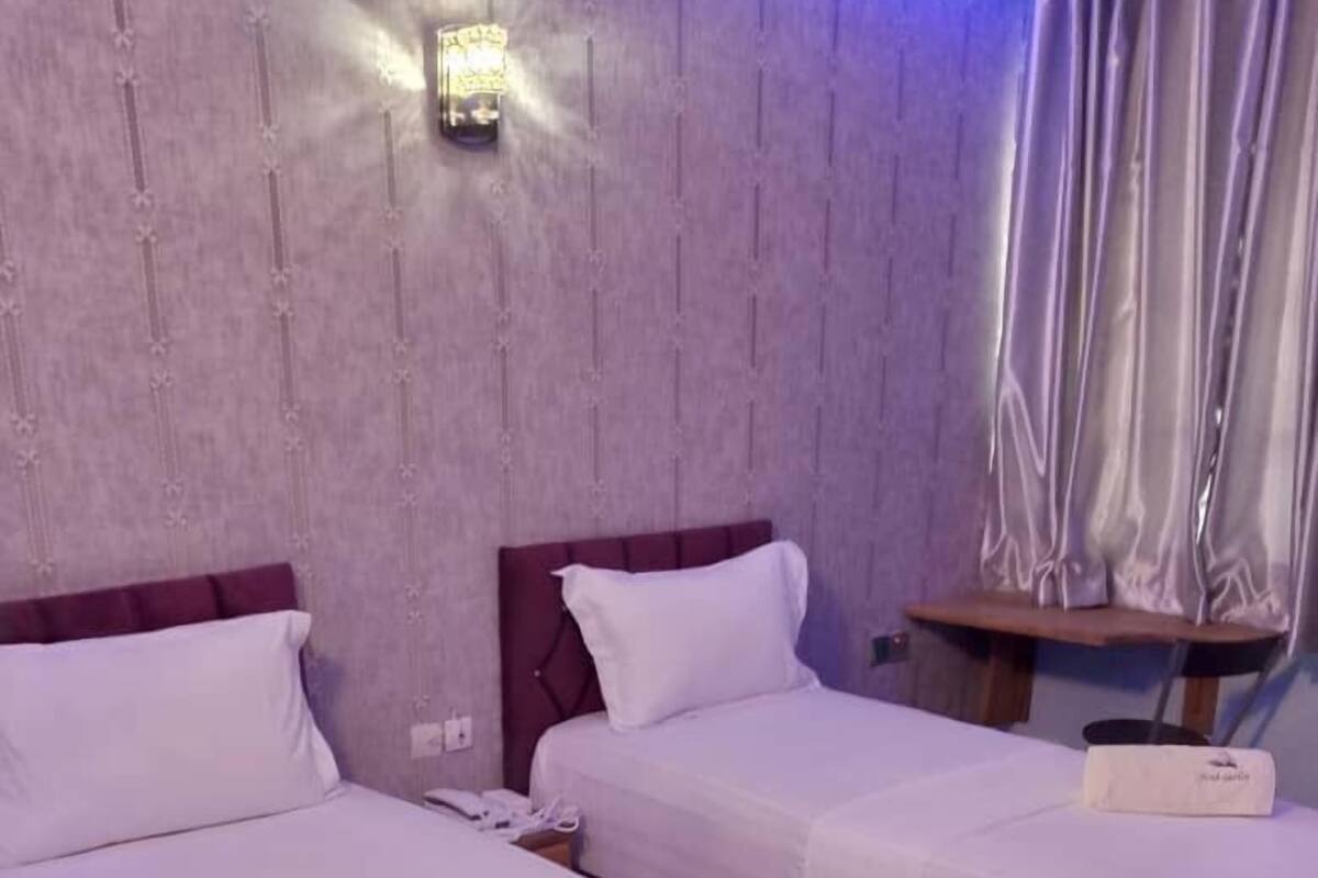 A hotel room with three single beds, a small table, and a wall-mounted light fixture.