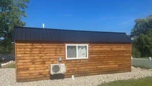 A small wooden cabin with a metal roof, a window, and an air conditioning unit.