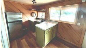 A compact kitchen with wooden walls, a built-in sink, and a refrigerator.