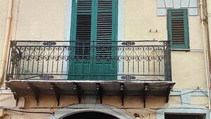 Un edificio de varios pisos con balcones, contraventanas verdes y una gran entrada en arco.