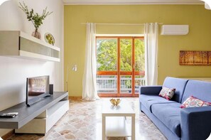 A living room with a sofa, a coffee table, a TV on a stand, a window with curtains, and a balcony with a railing. - Sampolo 70 - Central (Palermo)