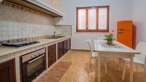 Una cocina con estufa, horno y lavamanos, una mesa de comedor con sillas, una ventana y un armario naranja.
