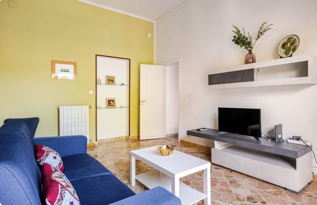 A living room with a blue sofa, a white coffee table, a TV on a stand, and a door leading to another room.