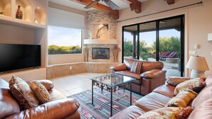 A spacious living room with a stone fireplace, leather sofas, a glass coffee table, and a large flat-screen TV. - Desert Oasis | TROON NORTH | Golf | Heated Pool (Scottsdale)