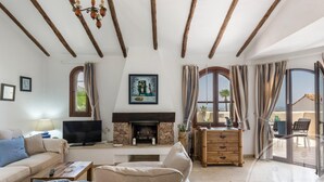 A living room with a fireplace, sofas, a television, and a balcony with outdoor furniture. - La Manga Club Los Altos Villa 367 (Atamaría)