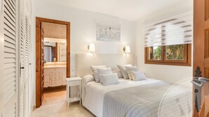 A bedroom with a bed, bedside tables, a nightstand, a window with blinds, a wall-mounted artwork, and a door with a wooden frame. - La Manga Club Los Altos Villa 367 (Atamaría)