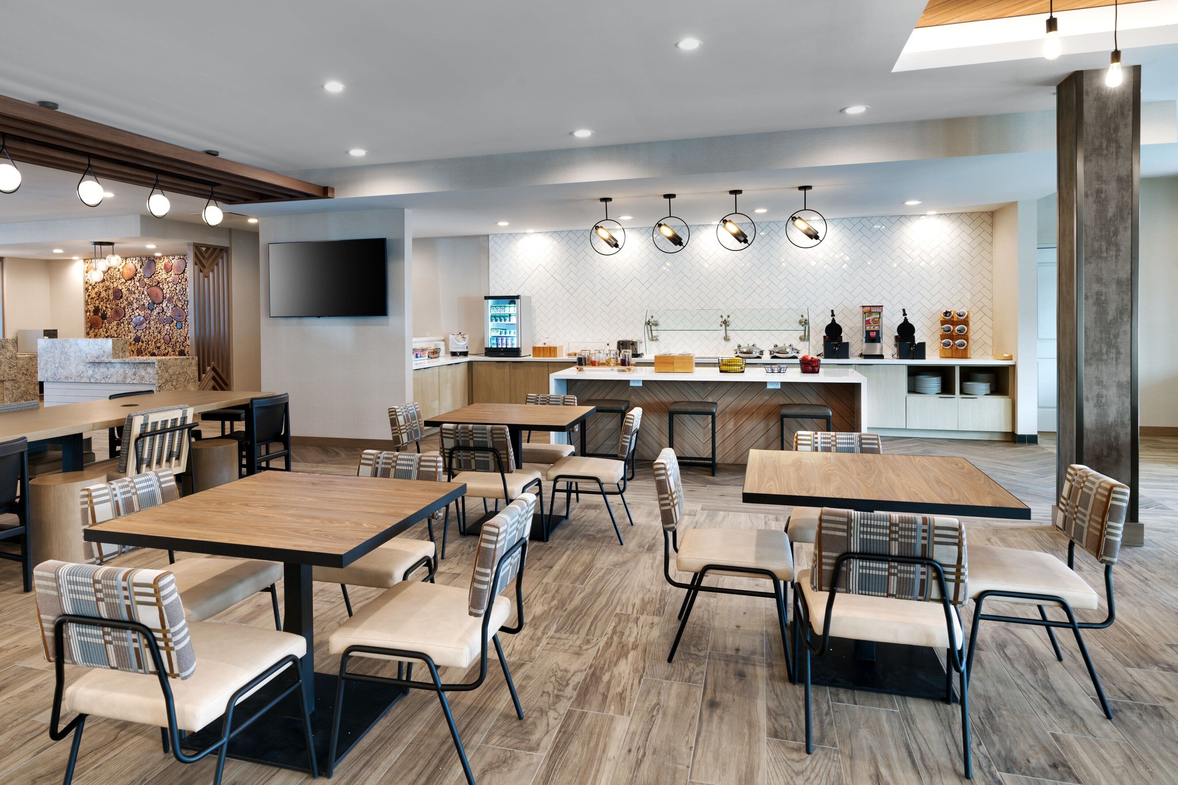 Un restaurante moderno con varias mesas y sillas, una zona de cocina y un televisor de pantalla plana montado en la pared.