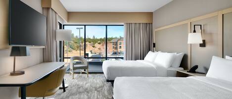 A hotel room with a large bed, a desk with a chair, a TV, and a view of the city.