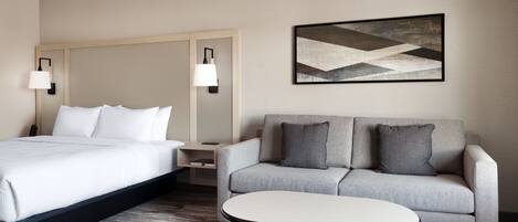 A hotel room with a bed, a sofa, a small table, and a wall-mounted lamp.