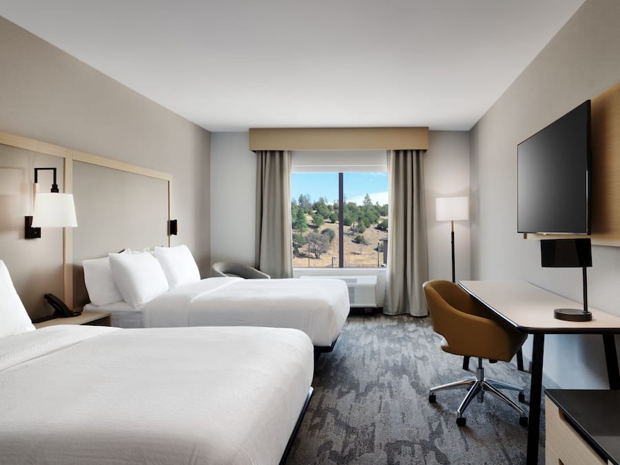 A hotel room with two beds, a desk, a chair, a TV, and a window with curtains.