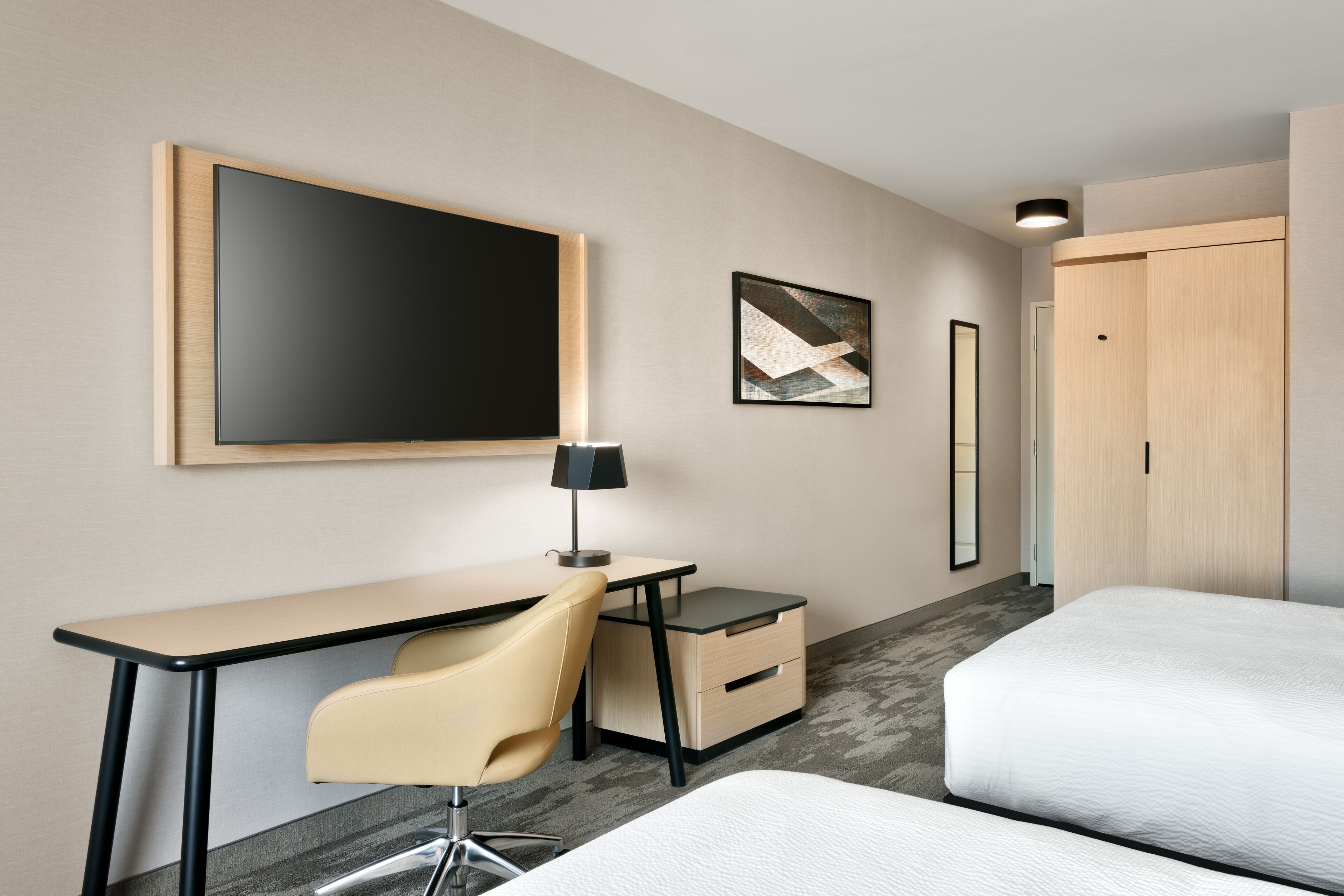 A hotel room with a desk, chair, bed, and artwork on the walls.