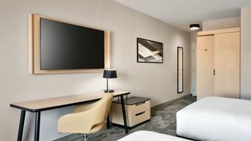 A hotel room with a desk, chair, bed, and artwork on the walls.