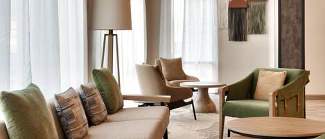 A modern hotel lobby with a sofa, armchairs, a floor lamp, and a round table.