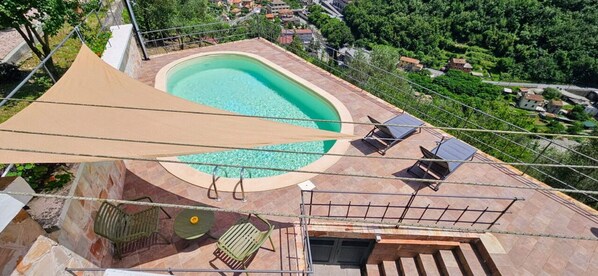 Una piscina en la azotea con agua azul cristalina, rodeada por una solana con baldosas y un toldo grande que ofrece sombra.
