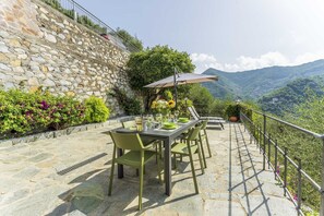 Terraza de piedra con una mesa lista para comer, con vistas a un paisaje montañoso.