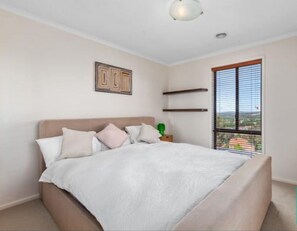 Relax in this serene bedroom with a large bed, green plant, and city view.