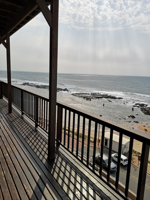 Una terraza de madera con barandilla que da a una playa rocosa y al océano.