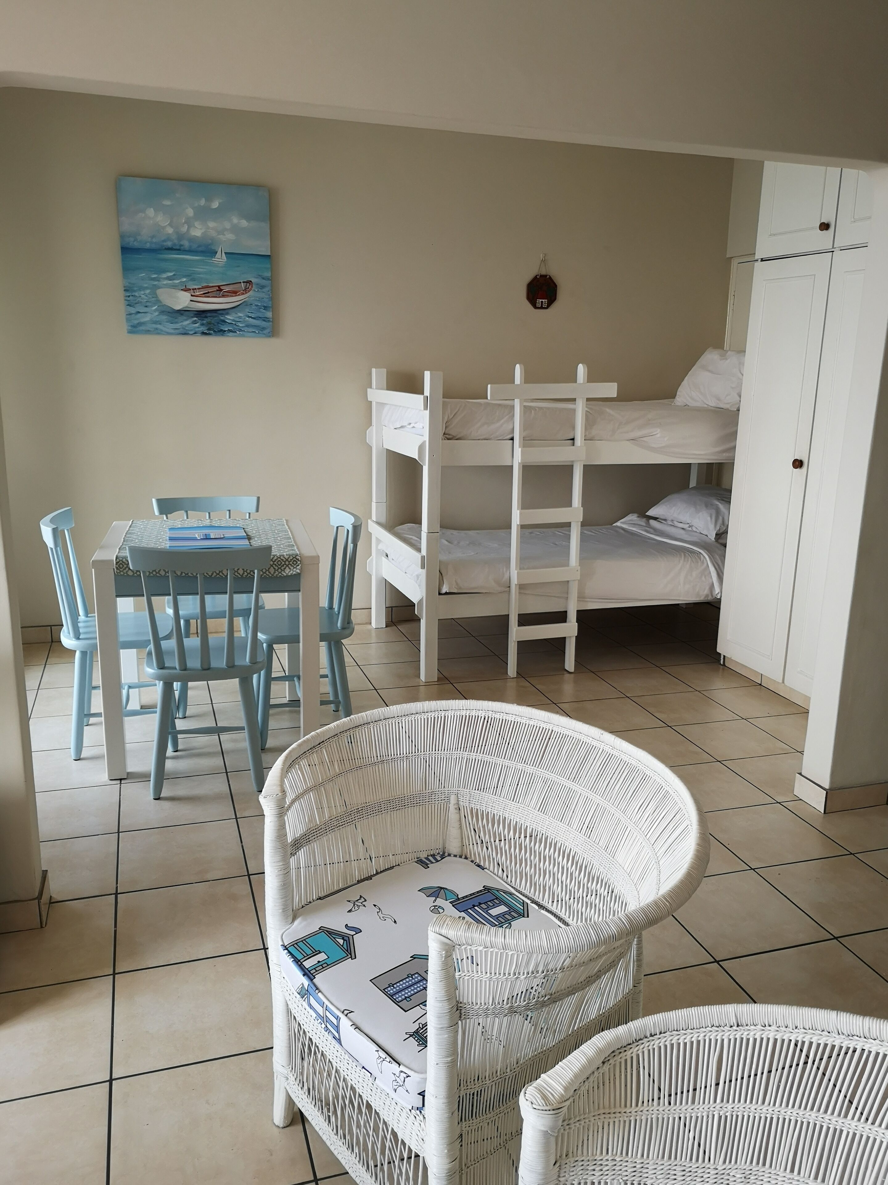 Una habitación con literas, una mesa de comedor con sillas y una silla de mimbre.