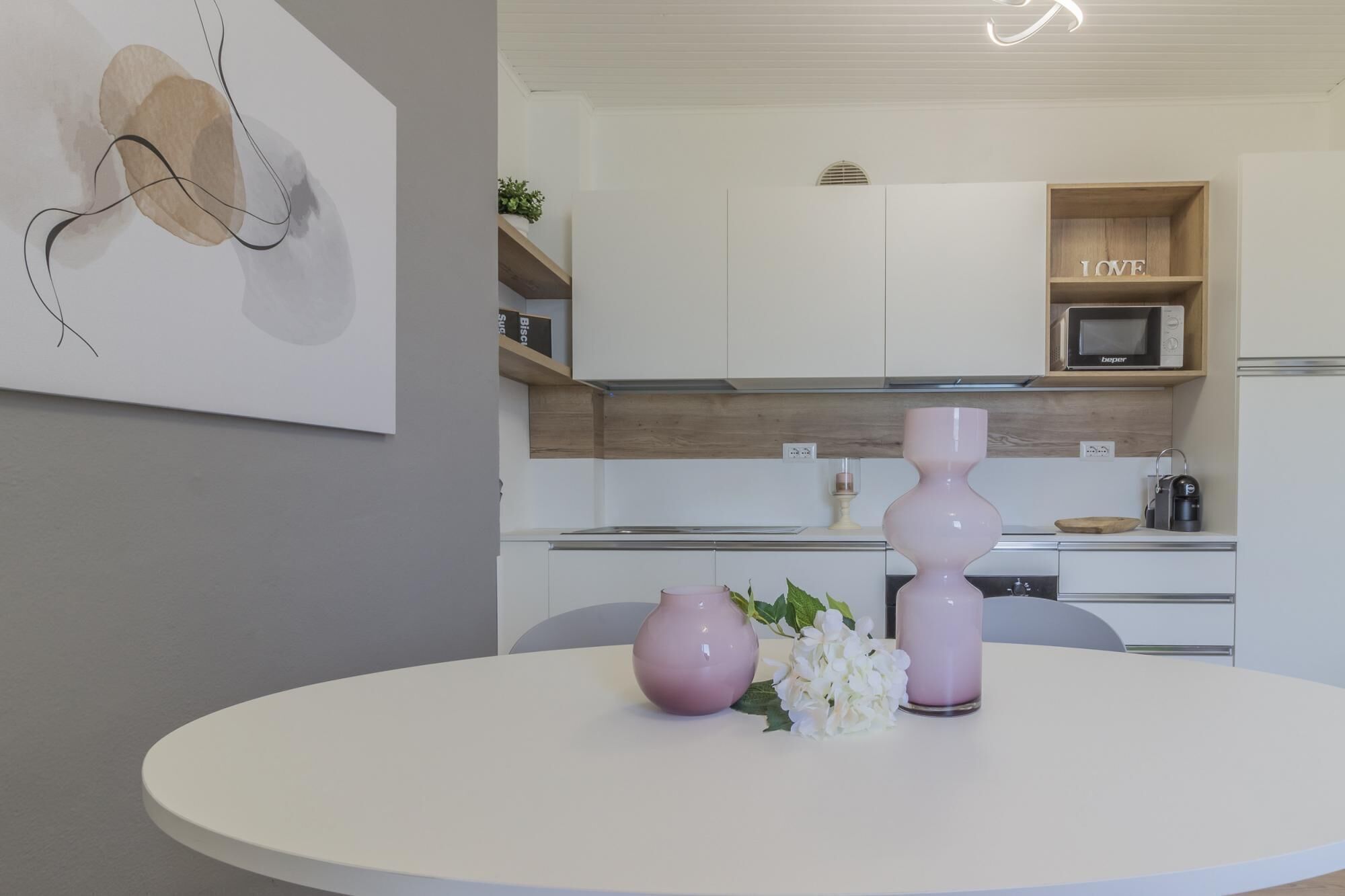 A modern kitchen with white cabinets, a wooden shelf with a 'LOVE' sign, a microwave, and a coffee machine.