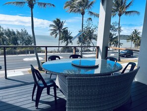 A round table with chairs on a balcony overlooking a street and palm trees.
