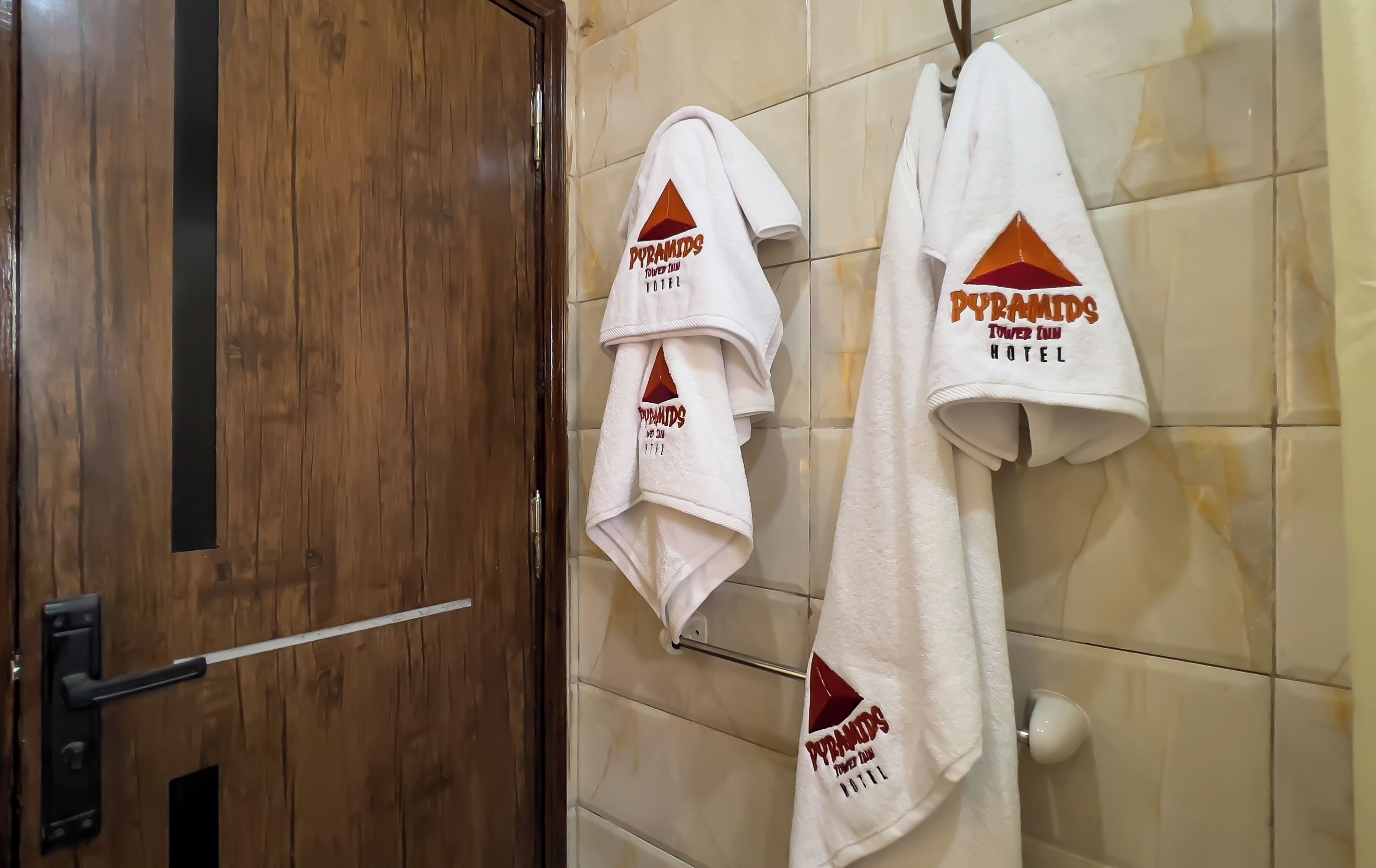 Une salle de bain avec des portes en bois, des murs carrelés et des serviettes suspendues à un porte-serviettes portant l’inscription « Pyramids Tower Inn ».