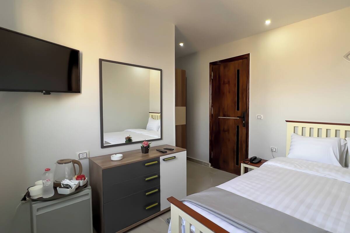 A hotel room with a bed, bedside table, mirror, wardrobe, and a door.