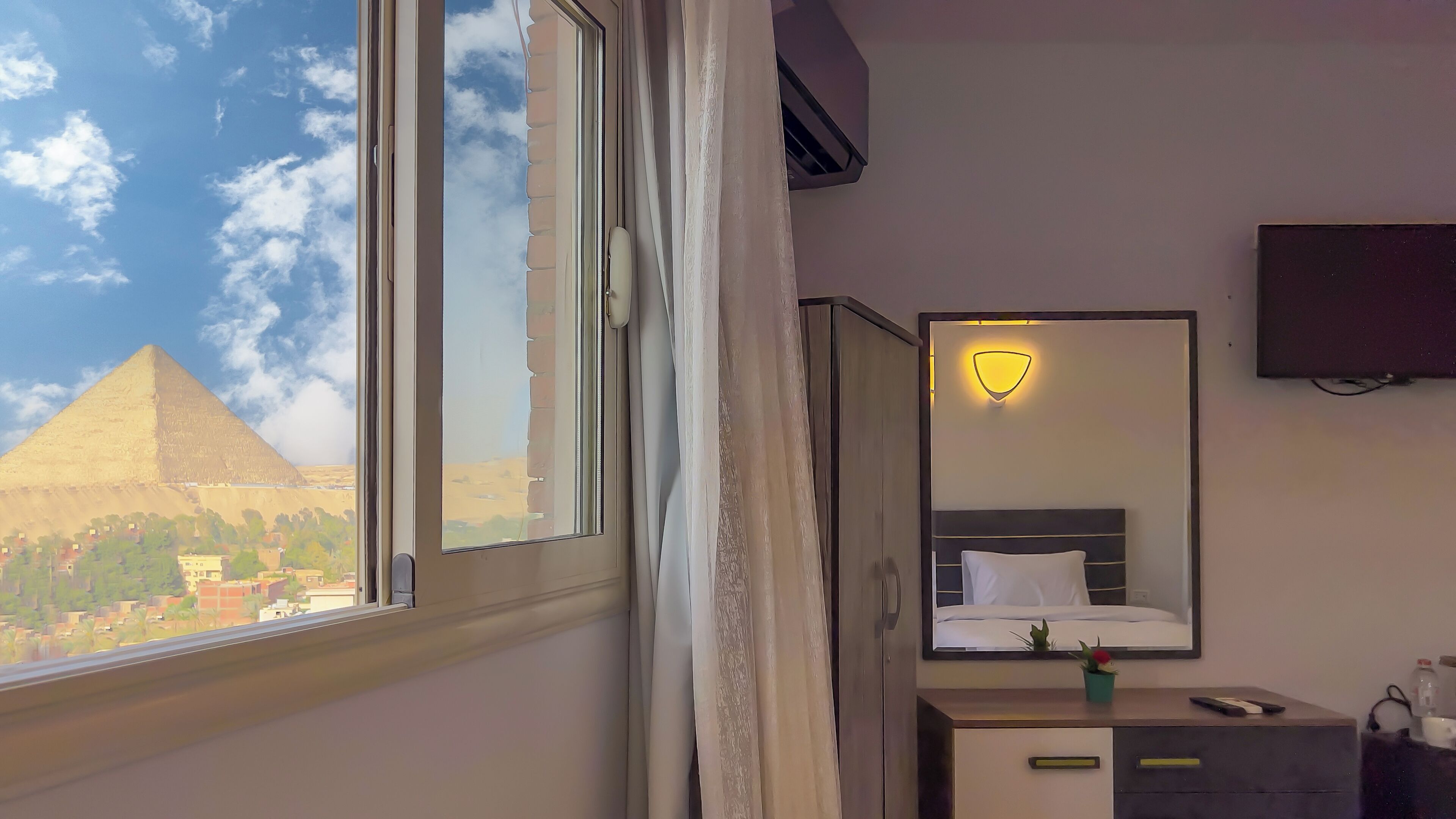 Une chambre d’hôtel dotée d’une grande fenêtre, d’un lit, d’une table de chevet, d’un miroir, d’un téléviseur fixé au mur et d’un luminaire fixé au mur.