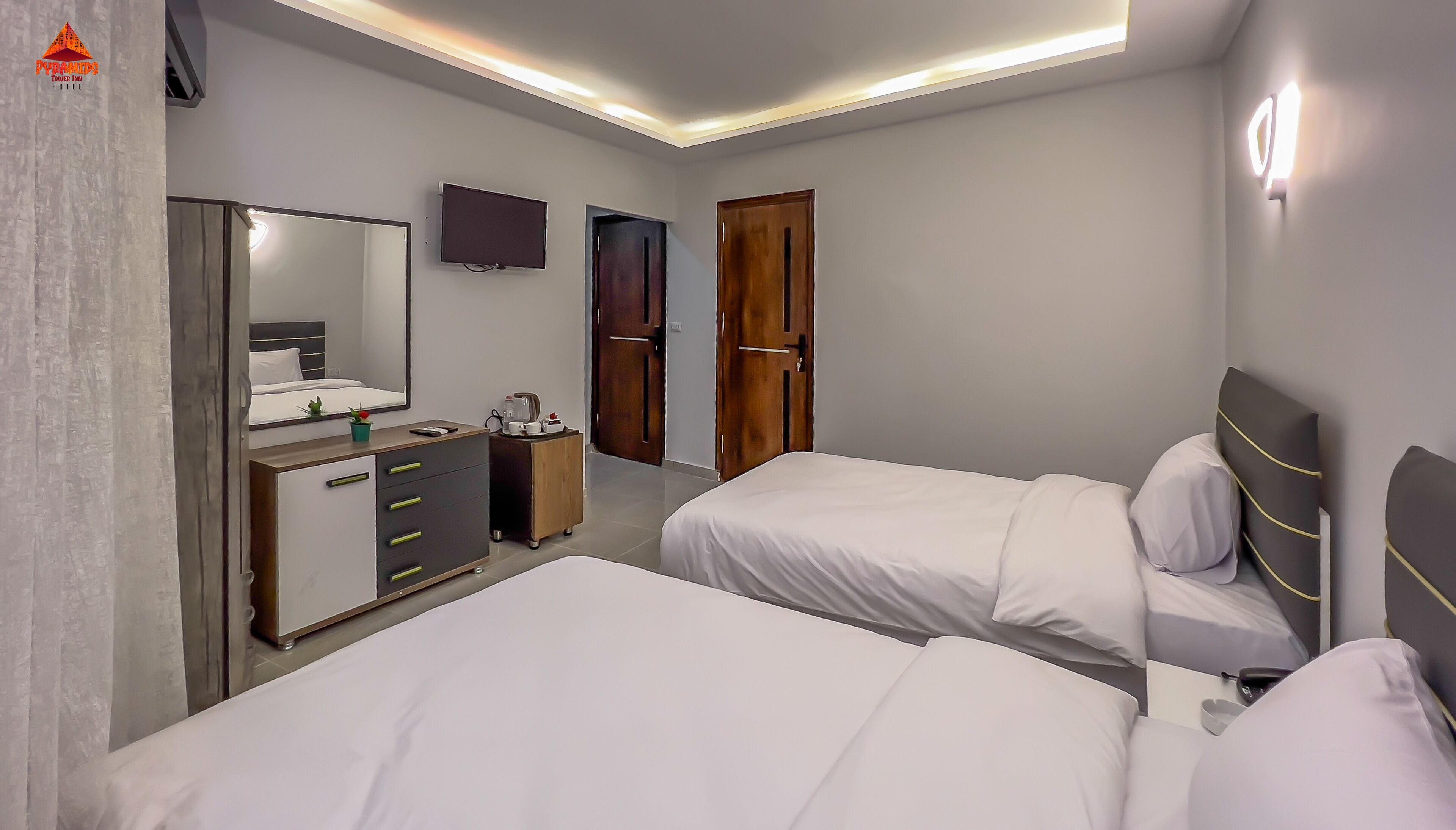 A hotel room with two beds, a dresser, a mirror, a television, and a door.
