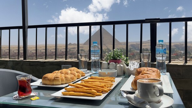 A table with pastries, a teapot, and water bottles, overlooking a mountainous landscape. - pyramids tower view inn (Giza)