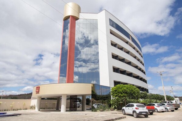 A modern hotel with a curved facade, a prominent red and beige tower, and a parking area with several cars. - Nobile Hotel Araripina (Araripina)