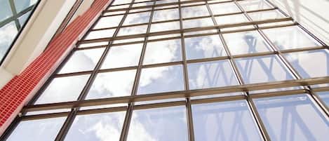 A view through a large window with a grid pattern, leading to a high ceiling and a visible sky.