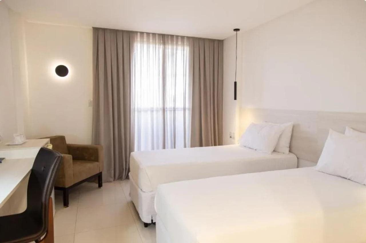 A hotel room with a bed, a desk, a chair, and a window with curtains.