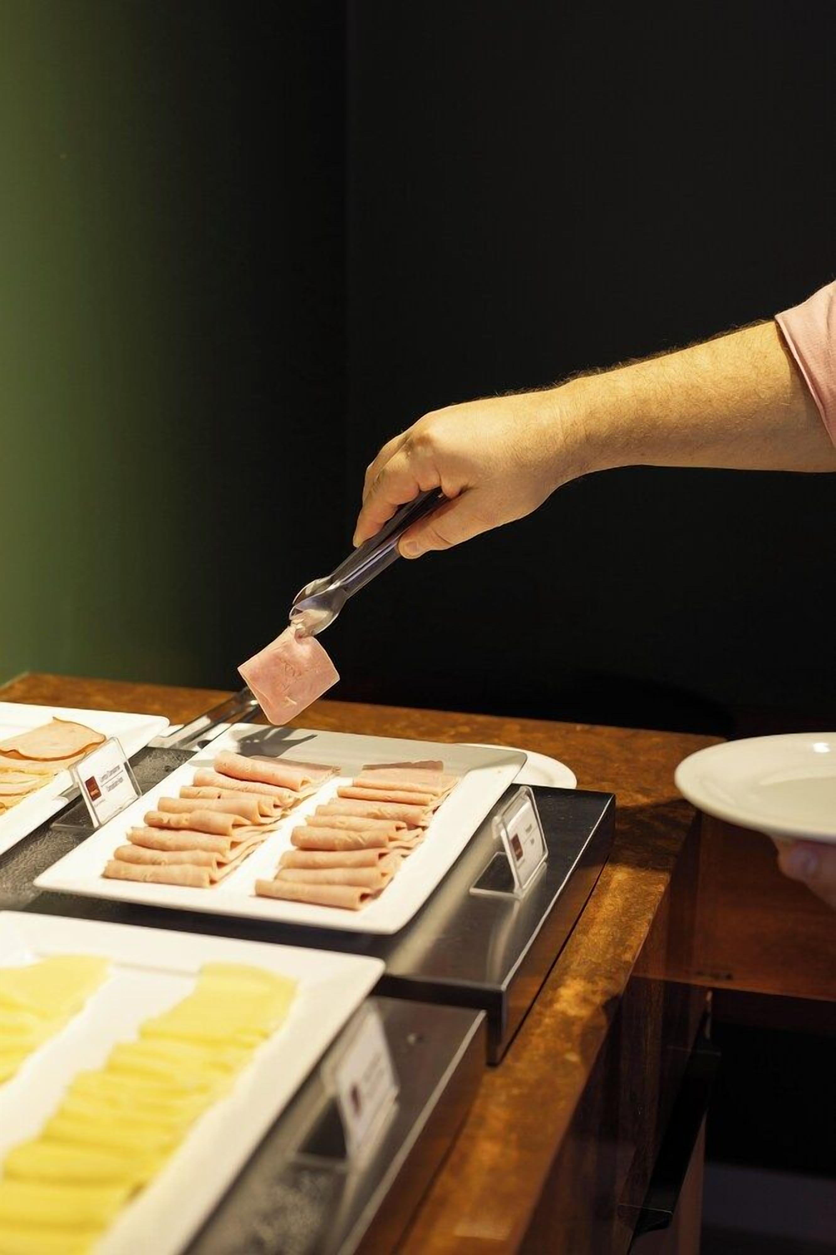 A person using tongs to serve food from a buffet.