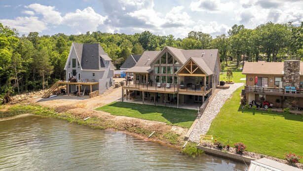 Una propiedad junto al lago con varias construcciones, incluyendo una casa grande con terraza y una cabaña más pequeña.