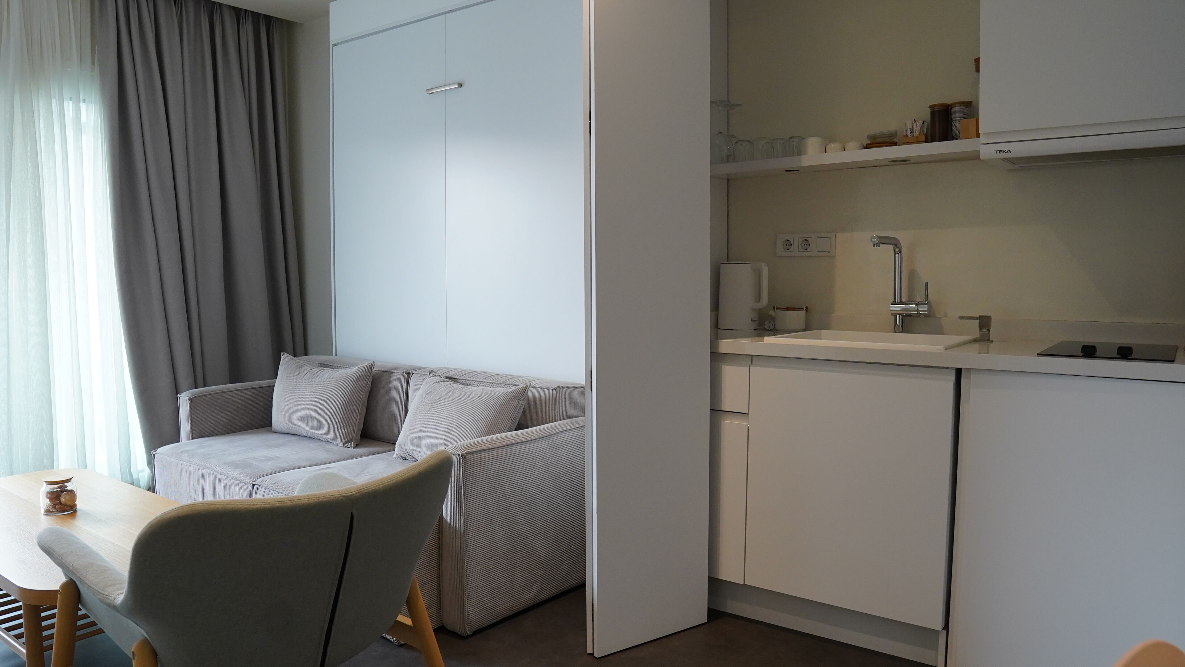 A modern kitchenette with a built-in oven, a sink, and a coffee maker.
