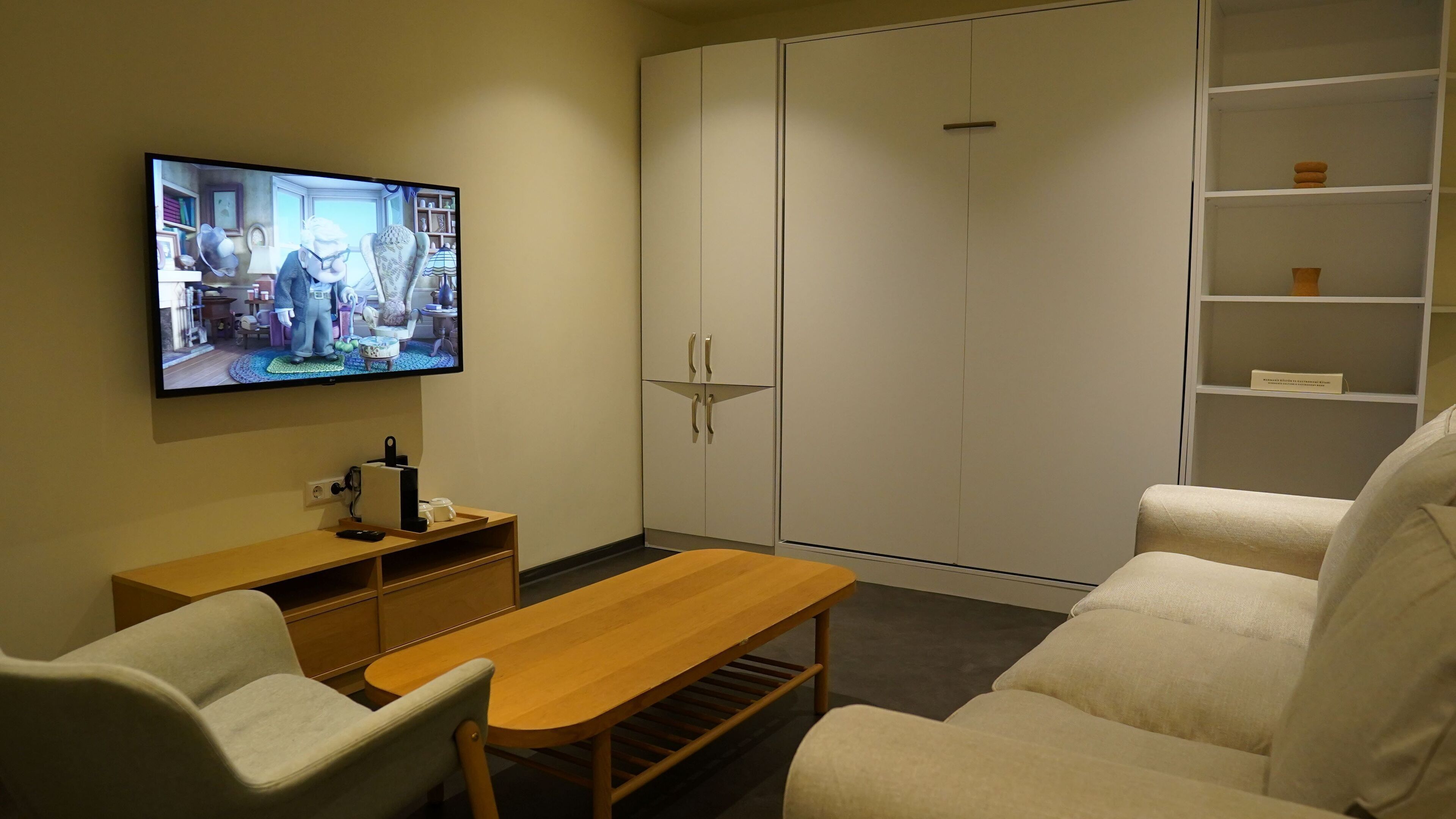 A living room with a TV, a wooden table, a sofa, and a wardrobe.
