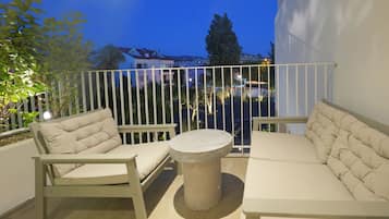 Un balcon doté d’une balustrade en métal blanc, de sièges beiges rembourrés et d’une table ronde.