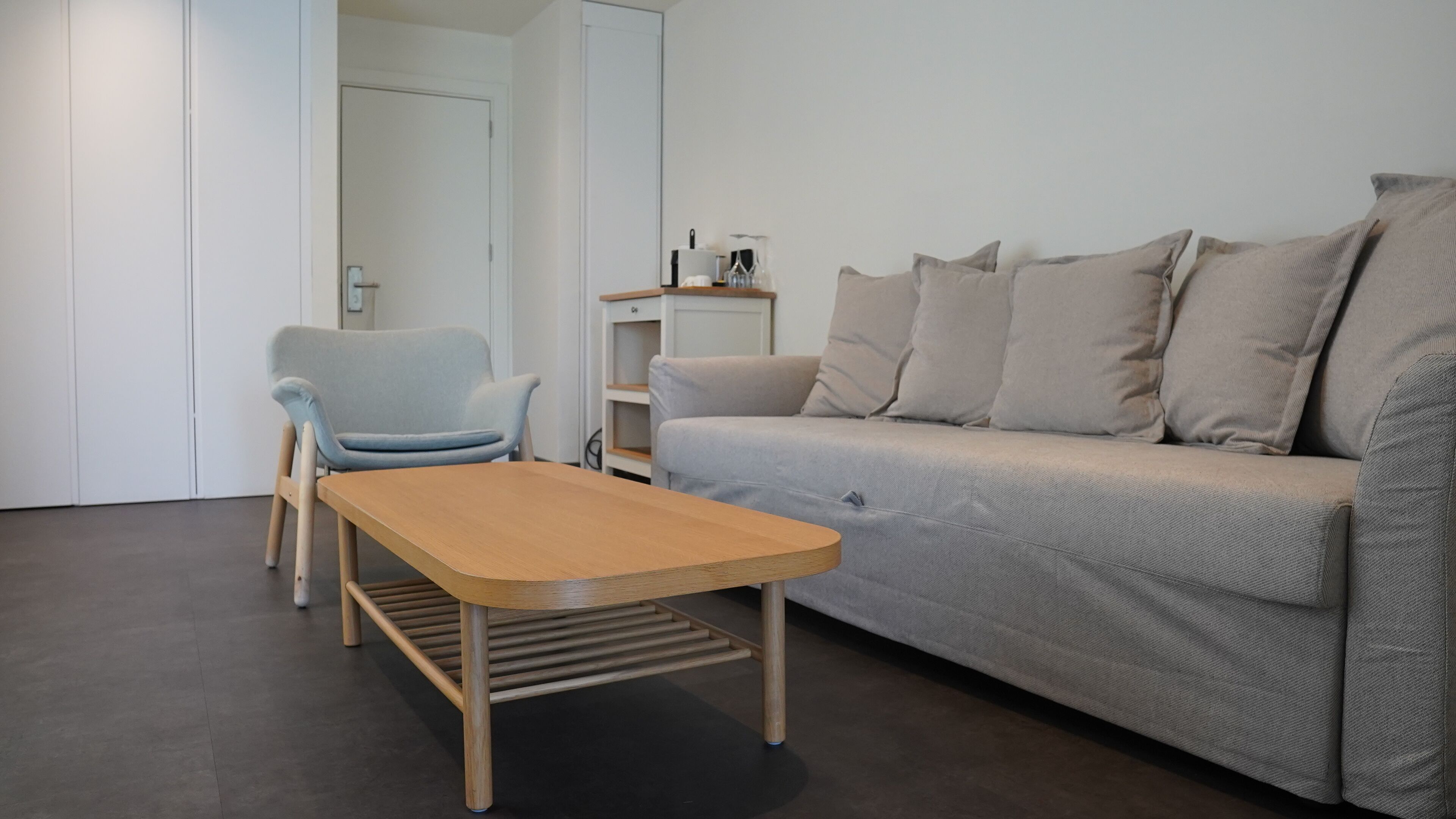 Una sala de estar moderna con un sofá gris, un sillón azul claro y una mesa de centro de madera.