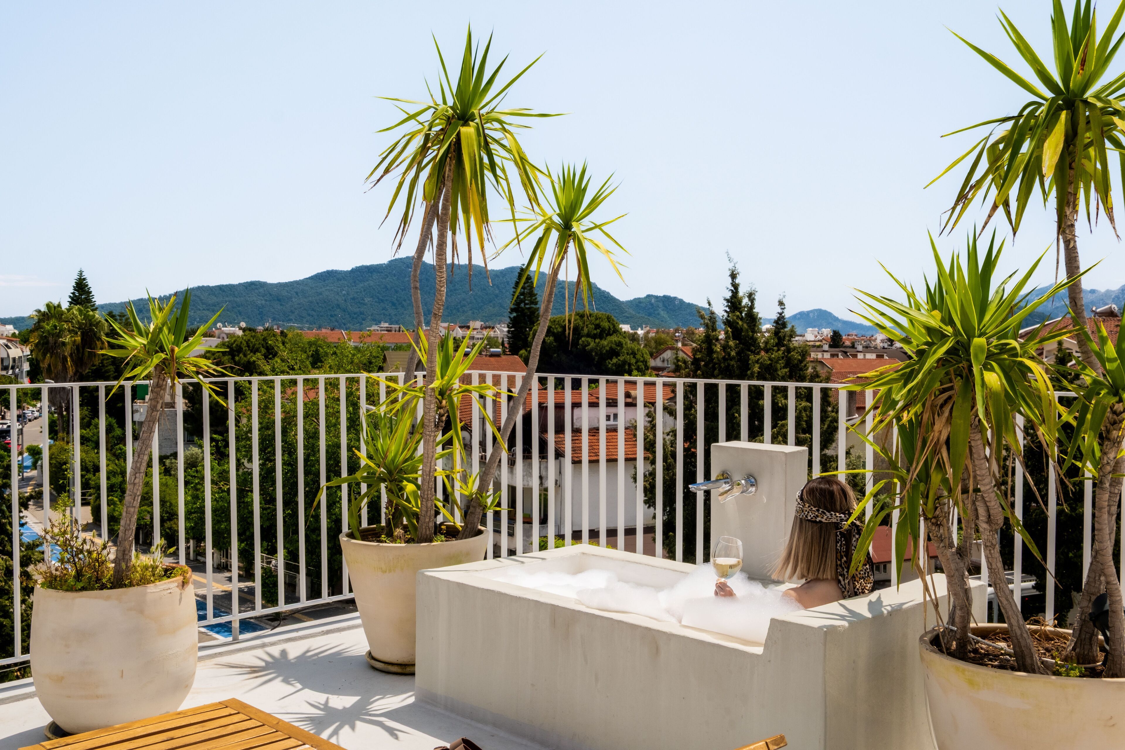 Une terrasse sur le toit avec un jacuzzi, des plantes en pot et une vue sur le paysage urbain et les montagnes.