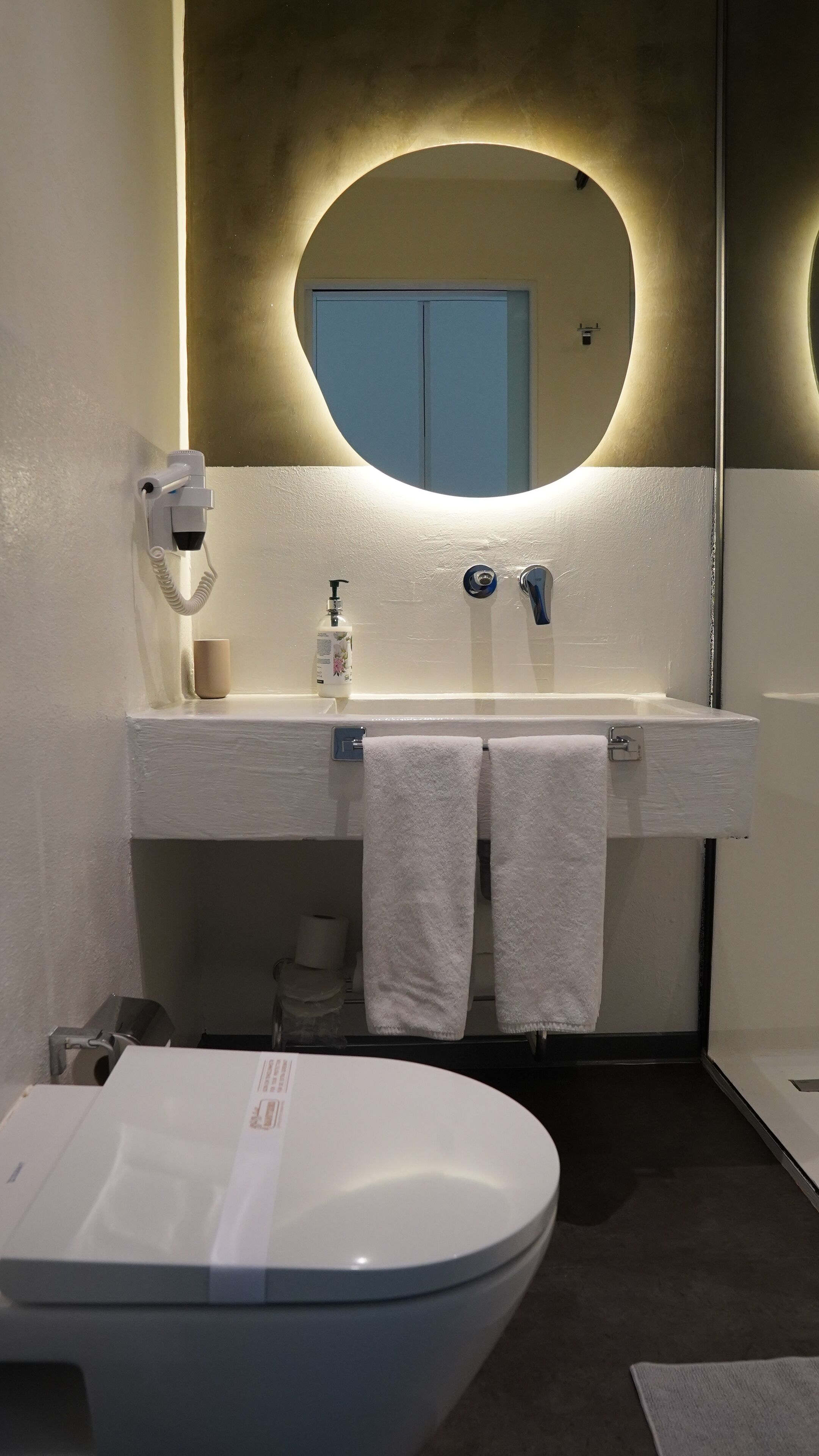 A modern bathroom with a white sink, a mirror, a toilet, and a towel rack.